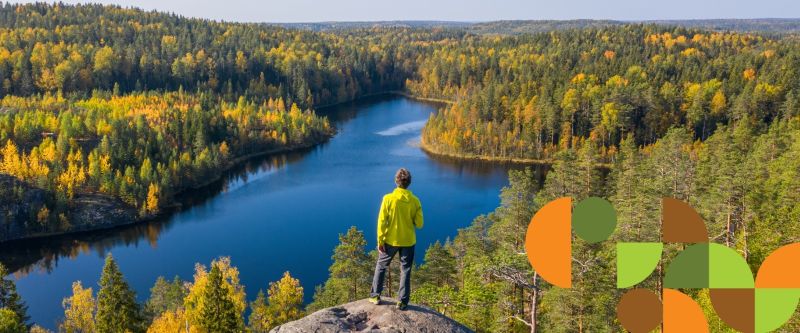 Syksyinen maisemakuva miehestä (oletettu), joka seisoo korkean kallion päällä katselemassa horisonttiin. Miehen lisäksi kuvassa näkyy etäällä alhaalla vesialue ja ruskan värisiä puita sekä kaistale sinistä taivasta.