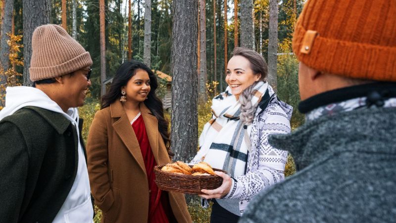 Syksyisen metsän keskellä henkilö tarjoaa pullia kolmelle muulle henkilölle.