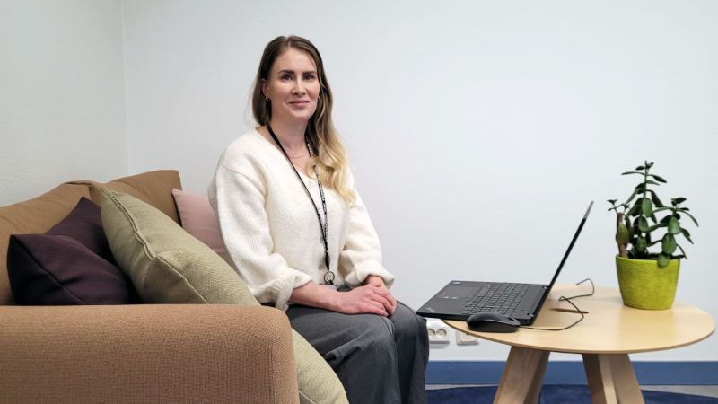 Henkilö istuu sohvalla pöydän ääressä, tietokone on pöydällä