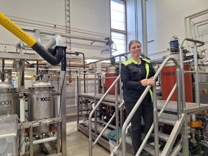 Kuvassa naispuolinen tuotantopäällikö hymyilee tehdastilan portaissa.