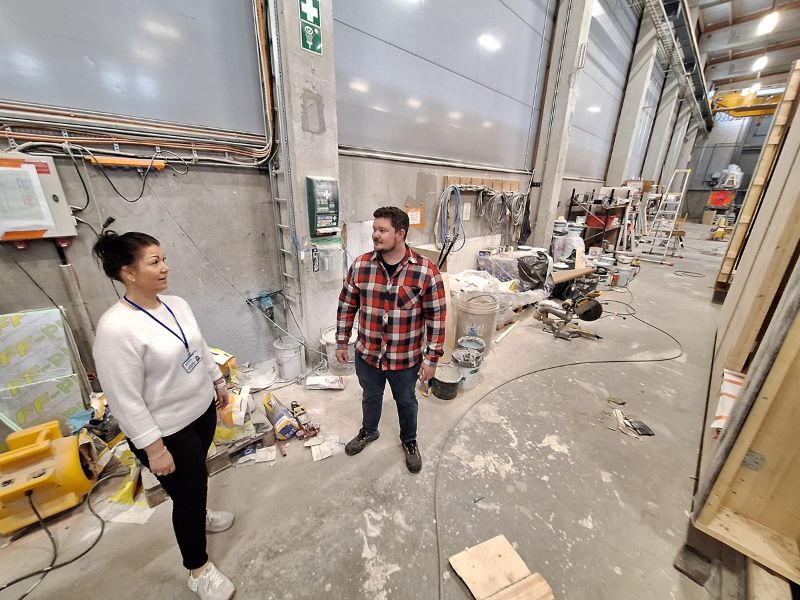 Kuvassa työhönvalmentaja Jenni Kenttä ja tehtaanjohtaja Mikko Huhta keskustelevat rakennushallissa.