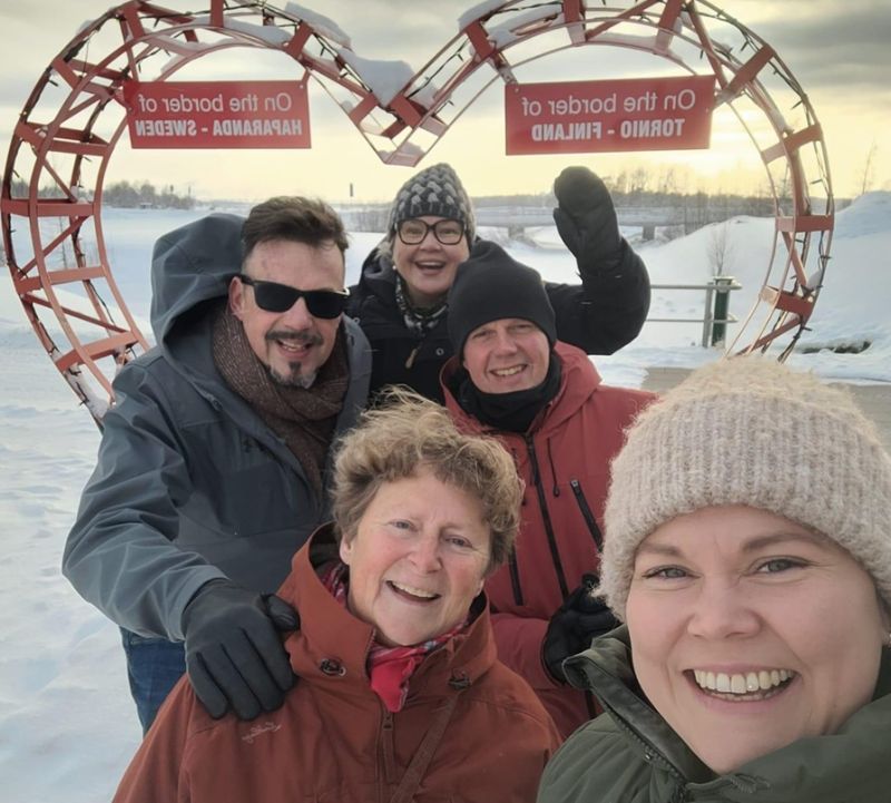 Ryhmä ihmisiä ottaa ulkona talvisessa maisemassa yhteiskuvaa. Taustalla näkyy luminen ympäristö ja rakenteita.