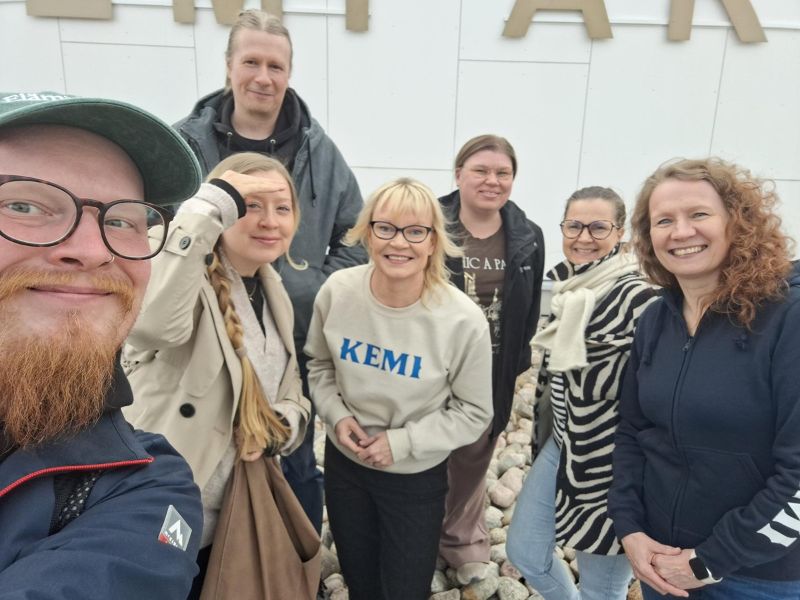 Kuvassa on joukko hymyileviä ihmisiä Kemi Areenan edustalla.