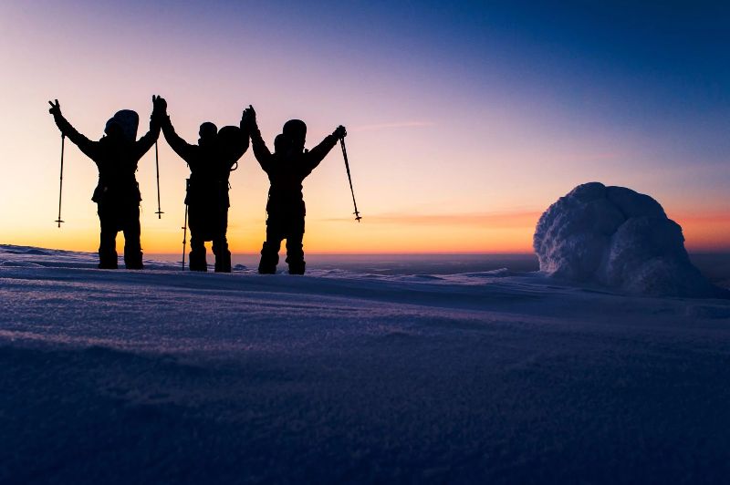 Lumilautailijat kaamosvaloisessa lumisessa tunturissa.