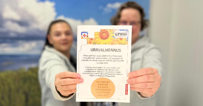 Kaksi henkilöä esittelevät uravalmennuksen esitettä.
