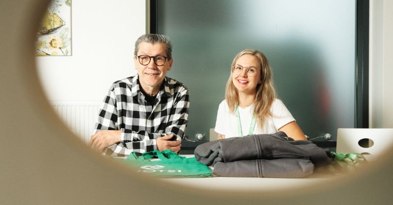 Työntekijät hymyilevät pöydän ääressä istuessaan.