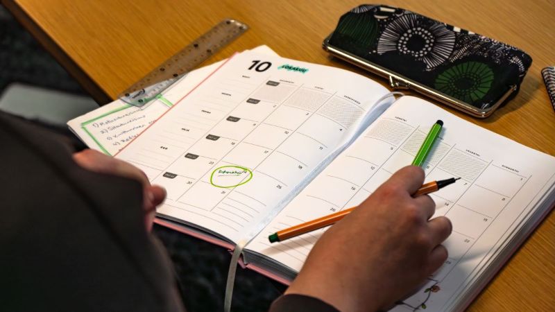 Kuvituskuva. Kuvassa on pöydällä avonainen kalenteri, johon tehdään merkintöjä.