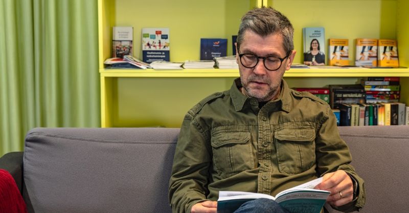 Henkilö opiskelee ja lukee kirjaa sohvalla.