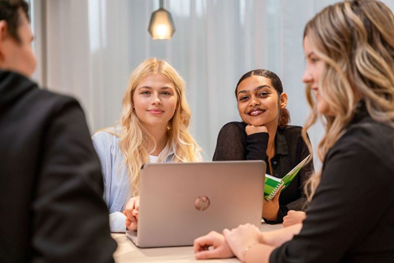 Opiskelijat istuvat pöydällä olevan tietokoneen ympärillä. 