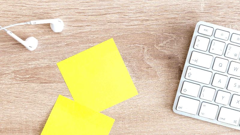 Nappikuulokkeet, muistilappuja ja näppäimistö puupöydällä.
