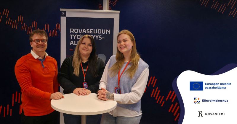 Hankkeen työntekijät Juho, Henriikka ja Satu valkoisen pyöreän pöydän ääressä katsovat hymyillen kameraan. Taustalla on tummansininen seinä ja Rovaseudun työllisyysalue -rullajuliste.