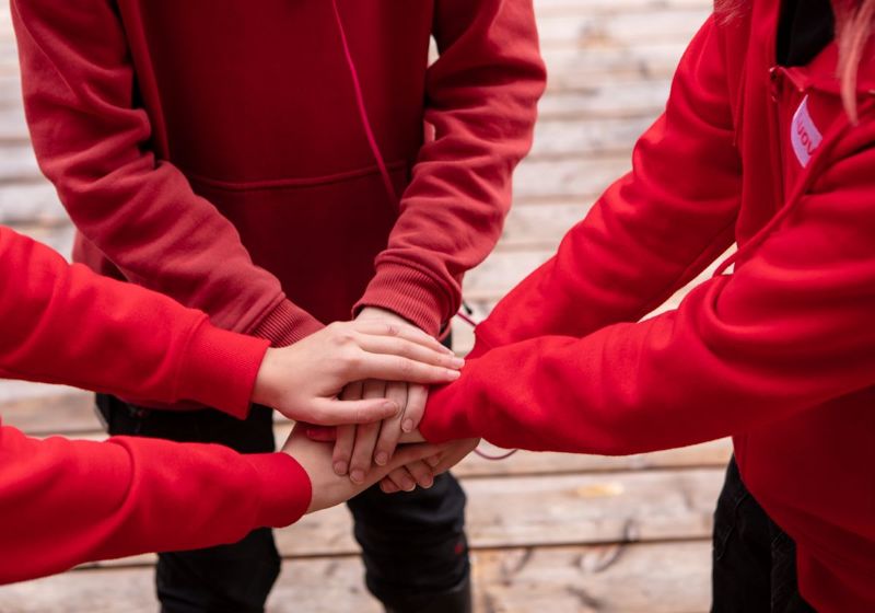 Kolmen Luovin punaisiin huppareihin pukeutuneen henkilön kädet yhteenliitettyinä.