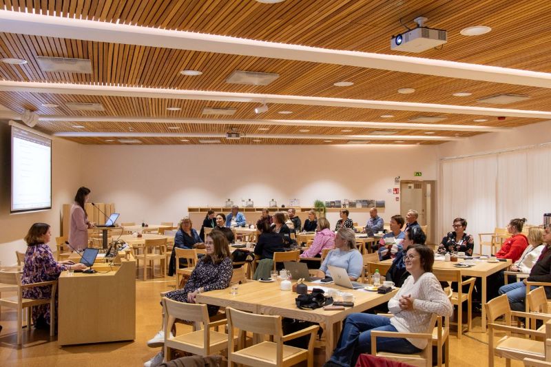 Tilaisuuden osallistuja Arktikumin Aurora-salissa istumassa pöytien ympärillä ja seuraamassa valkokankaalle heijastettua esitystä.