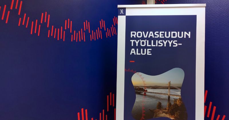 Rovaseudun työllisyysalue -rullajuliste, jonka taustalla on tummansininen seinä, johon on koristeeksi maalattu punaista, revontulia muistuttavaa symbolinauhaa.