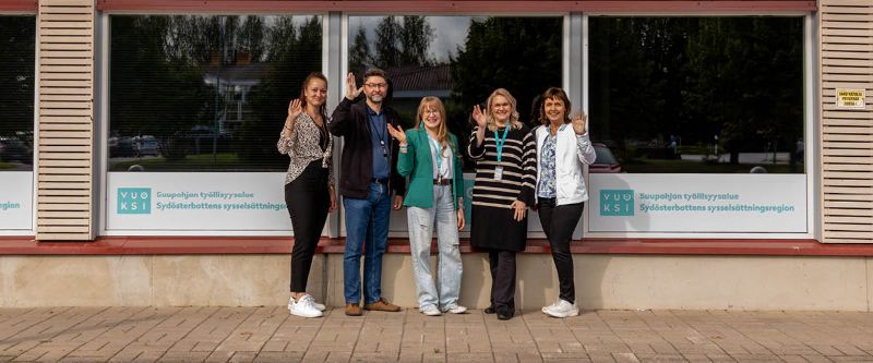 Suupohjan työllisyysalueen työntekijät seisovat rivissä ulkona toimiston edessä hymyilemässä ja heiluttamassa.