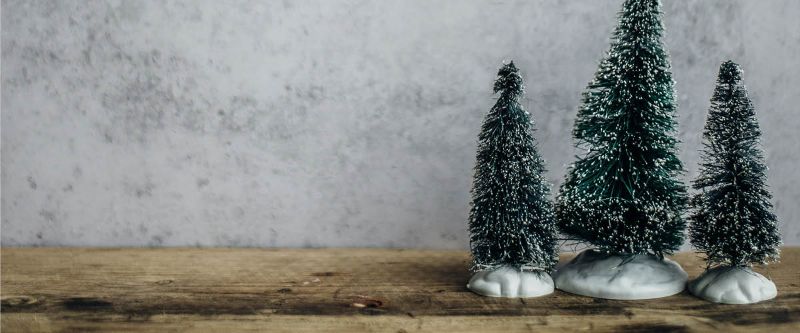 Kolme pientä koristejoulukuusta puisella pöydällä.