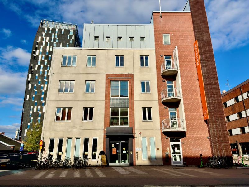 Viisikerroksinen kivitalo kuvattuna edestäpäin. Taustalla korkea Torni-hotelli.