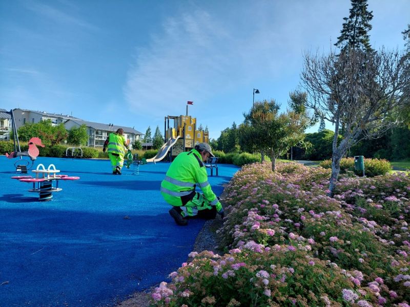 Työasuihin pukeutuneet henkilöt tekvät puutarhatöitä lasten leikkipuistossa.