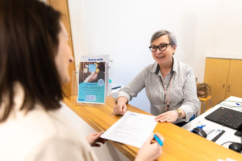 Asiakaspalvelija ojentaa asiakkaalle lomakkeen.