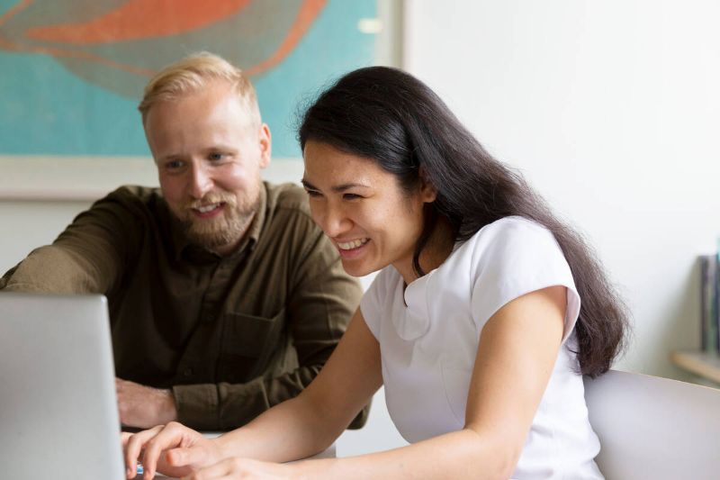 Kaksi henkilöä istuu tietokoneen ääressä hymyillen.